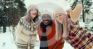Three multiethnic fun happy serene friends wave, smile at camera posing at beautiful snowy winter forest slow motion.