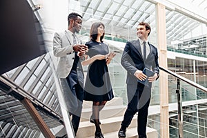 Three multiracial business people walking down on stairs with digital tablet