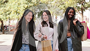 Three multiracial happy young women walking and talking on a shopping day. Group of girls carrying bags smiling on the