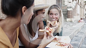 Three multiracial women eating pizza enjoying holidays together in Italy