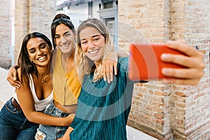 Three multiracial young friends having fun taking self portrait with cell phone