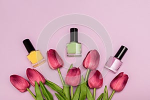 Three nail polish bottles: green, yellow and pink with fresh spring tulip flowers on a pink background