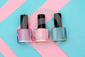 Three nail polish bottles on striped pink and blue background. Pink and red nail polish bottle on striped background. Copy space