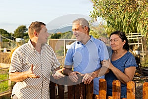 Three neighbours farmers talking together near wooden fence in garden