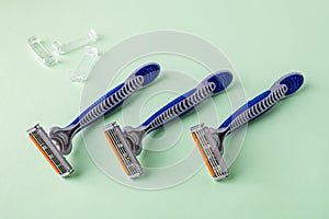 Three new disposable shaving razors with triple blade lie in a row on a pastel green background. Silver blue plastic razor with