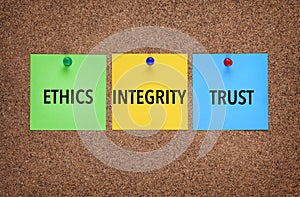 Three notes on corkboard with words Integrity, Trust, Ethics.