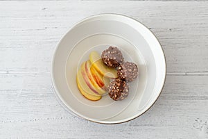 Three Nutty Clustered Chocolate Ice Cream Balls and Sliced Apple in a brown Serving Bowl on White Painted Wooden Boards