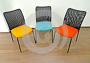 Three office chairs with color seats stand indoors