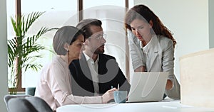 Three office employees gather at workplace using laptop