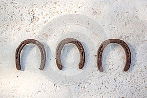 Three old rusty horseshoes hanging on a white wall, luck symbol