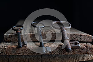 three old rusty keys lie on old wooden board against a dark background