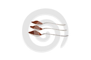 Three old silver spoons with ground coffee on a white background