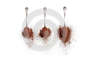 Three old silver spoons with ground coffee on a white background