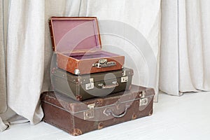 Three old suitcases on floor next to linen curtain