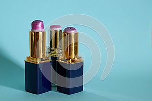 Three old used tubes of lipstick stand on a blue background.