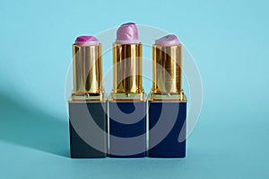 Three old used tubes of lipstick stand on a blue background.