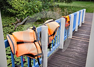 three orange life jackets on the lakeside bridge fence. Fishing water safety concept, misadventure