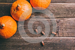 Three orange pumpkins and acorns on wooden background