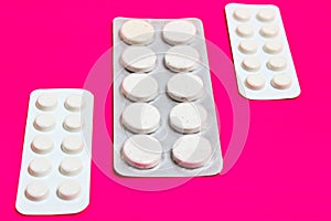 Three packs of pills lying on the pink background.