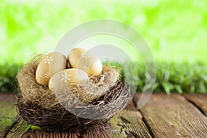 Three painted Easter eggs in the nest on table and green nature background