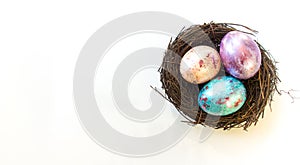 Three painted pearlescent easter eggs in a bird nest isolated on white