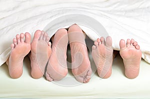 Three pairs of feet in bed