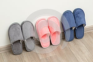 Three pairs of new home slippers stand on the grey floor near white wall