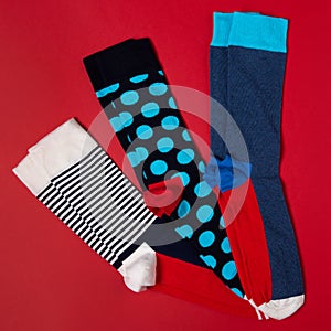Three pairs of stylish colored socks with patterns, on a red background, fashion concept
