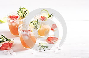 Three paloma alcoholic cocktails with ice and tequila, garnished with lime wedges, grapefruit and rosemary