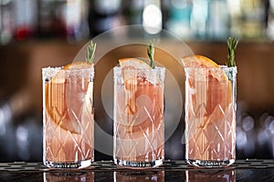 Three paloma cocktails garnished with grapefruit and rosemary placed on the bar counter