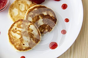 Three pancakes with cheese and strawberries and sauce on a white dish against wood background. Delicious cheese pancake and