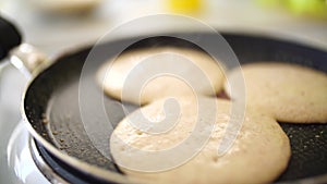 Three pancakes are fried in a frying pan, on an electric stove, against the background of the kitchen table.