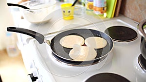 Three pancakes are fried in a frying pan, on an electric stove, against the background of the kitchen table.