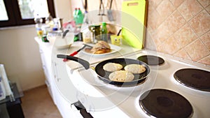 Three pancakes are fried in a frying pan, on an electric stove, against the background of the kitchen table.