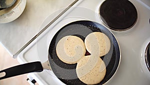 Three pancakes are fried in a frying pan, on an electric stove, against the background of the kitchen table.