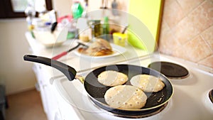 Three pancakes are fried in a frying pan, on an electric stove, against the background of the kitchen table.