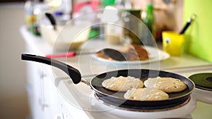 Three pancakes are fried in a frying pan, on an electric stove, against the background of the kitchen table.