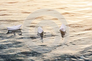 Three paper boats floating in waves on the water at sunset.
