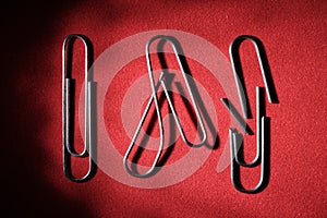 Three paper clips on a red background, whole, bent and broken. The concept of breaking the bonds
