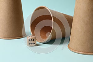 Three paper cups and dice on light blue background, closeup. Thimblerig game