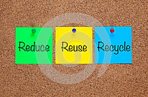 Three paper notes on corkboard with words Reduce, Reuse, Recycle