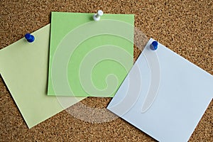 Three paper notes green, white and yellow color on a cork Board, attached with a white pushpin. Copy space