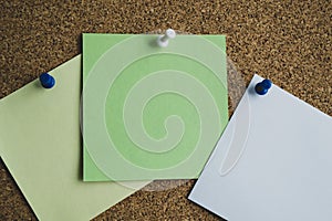 Three paper notes green, white and yellow color on a cork Board, attached with a white pushpin. Copy space
