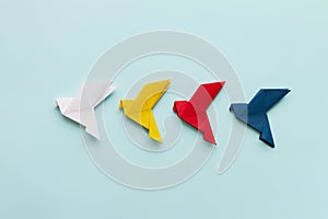 three paper origami pigeons white, ellow, red and blue in row on light background