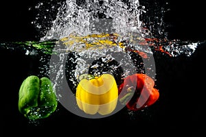 Three Paprika splash in water on black background, Capsicum annuum: bell pepper and buble