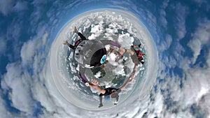 Three parachutists holding hands with a 360 degree camera.