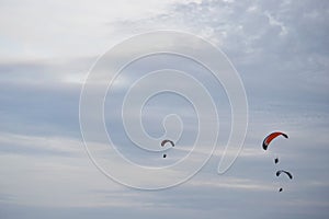 Three paragliders flying far away in a light cloudy sky in the summer