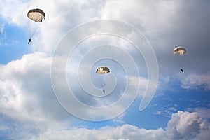 Three paratroopers jump with parachutes on the blue sky with white clouds background