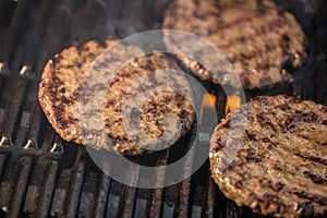 Three patties of ground meat on a cooking grate with flames and
