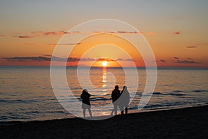 Three peolple walking on a beach under sunset